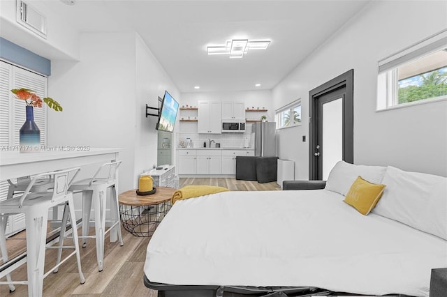 bedroom with multiple windows, stainless steel refrigerator, and light hardwood / wood-style flooring