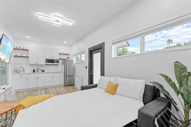 bedroom with multiple windows, sink, light hardwood / wood-style flooring, and stainless steel refrigerator