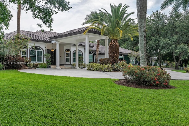 back of house with stucco siding, a tile roof, a lawn, and concrete driveway