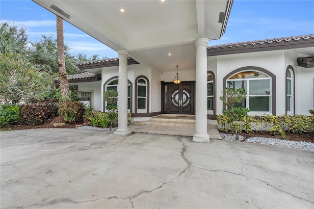 doorway to property featuring visible vents, a tiled roof, and stucco siding