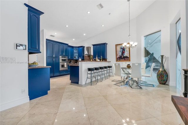 kitchen featuring wall chimney range hood, lofted ceiling, a breakfast bar, blue cabinets, and a notable chandelier