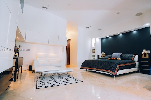 bedroom with an accent wall, a high ceiling, visible vents, and baseboards