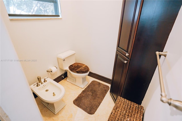 bathroom featuring toilet, a bidet, and baseboards
