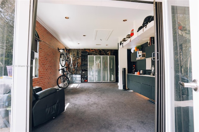 unfurnished room featuring attic access, carpet flooring, and brick wall
