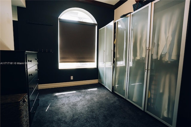 unfurnished bedroom featuring baseboards, dark carpet, and crown molding