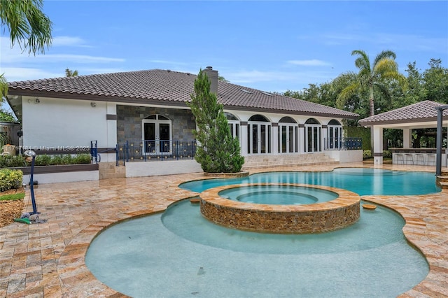 rear view of property featuring stone siding, french doors, a pool with connected hot tub, and a chimney