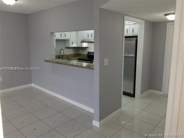 kitchen featuring stone counters, sink, black electric range, white cabinetry, and stainless steel refrigerator