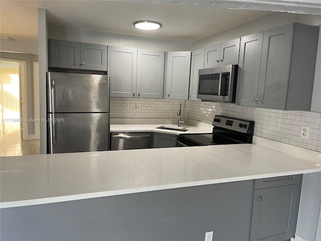 kitchen with appliances with stainless steel finishes, backsplash, light stone counters, sink, and gray cabinets