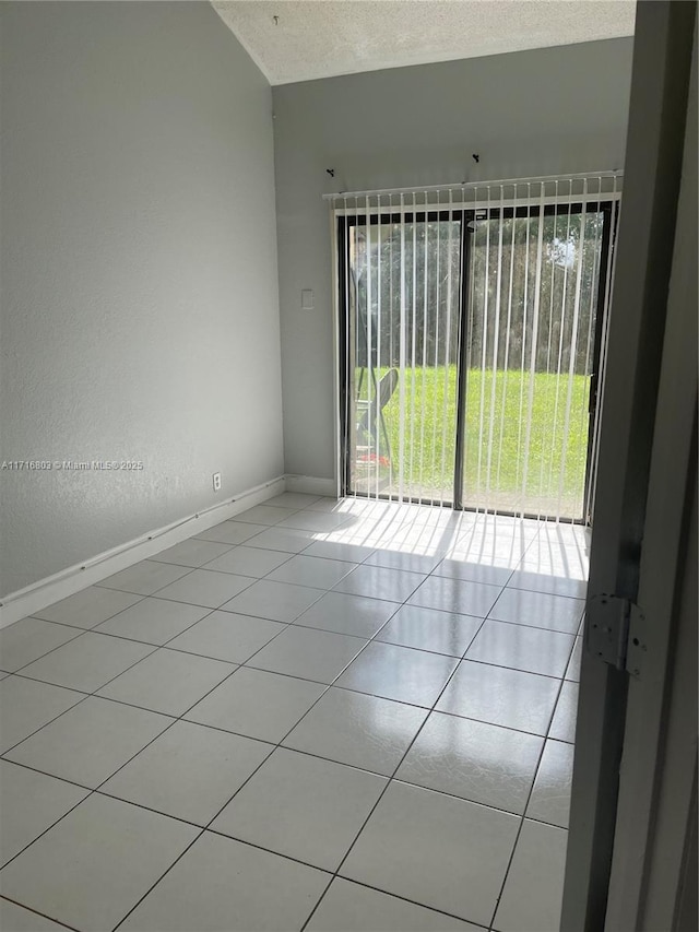 empty room with light tile patterned flooring, a textured ceiling, and vaulted ceiling