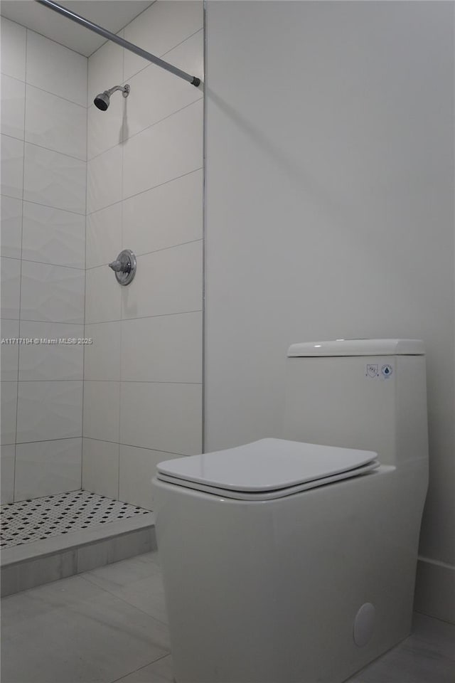 bathroom with tile patterned flooring, toilet, and a tile shower