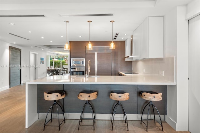 kitchen featuring tasteful backsplash, white cabinetry, a breakfast bar area, and decorative light fixtures