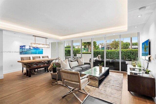 living room with a tray ceiling, floor to ceiling windows, and light wood-type flooring