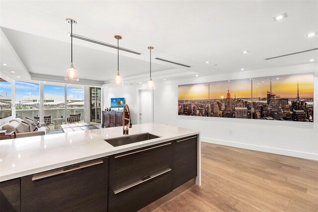 kitchen featuring pendant lighting, light wood-type flooring, sink, and a tray ceiling