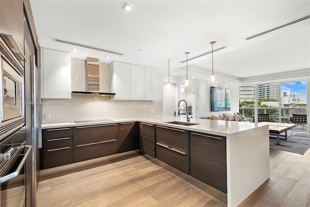 kitchen with sink, wall chimney exhaust hood, dark brown cabinets, white cabinets, and black appliances