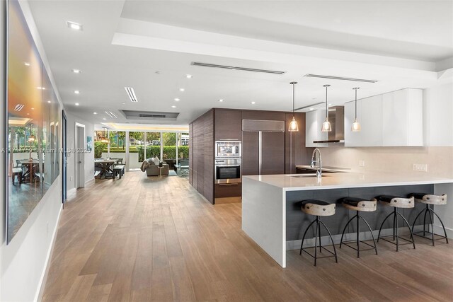 kitchen with white cabinetry, sink, hanging light fixtures, built in appliances, and light wood-type flooring