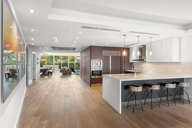 400 Alton Rd Unit 509, Miami Beach, FL 33139 - kitchen with modern cabinets, built in appliances, wall chimney range hood, light wood finished floors, and a breakfast bar area