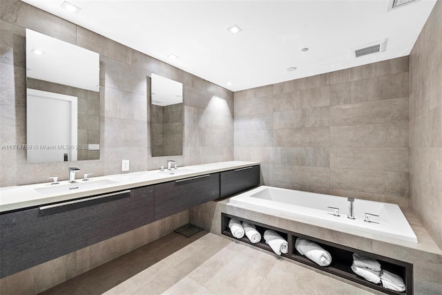 bathroom featuring tile patterned floors, vanity, tile walls, and tiled bath