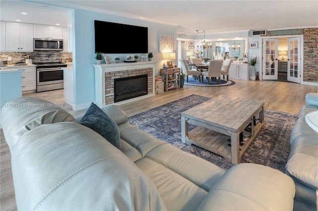 living room with french doors, light wood-type flooring, ornamental molding, an inviting chandelier, and a fireplace