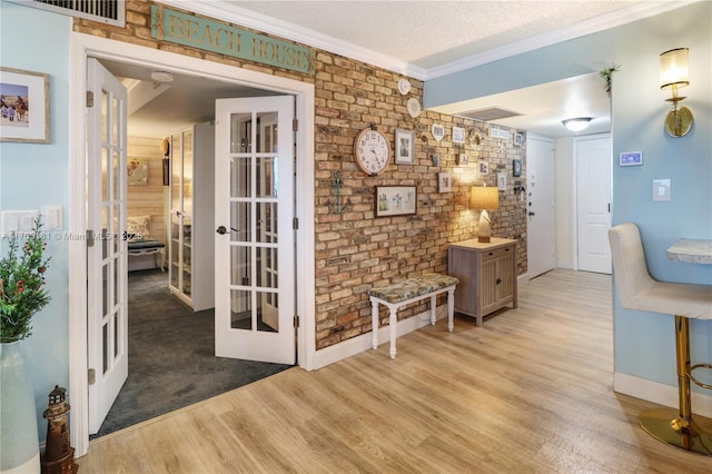 corridor featuring french doors, light hardwood / wood-style flooring, ornamental molding, a textured ceiling, and brick wall