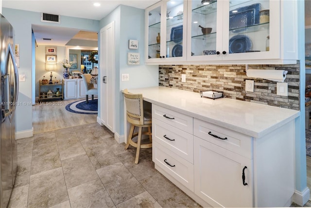 kitchen with stainless steel fridge with ice dispenser, light stone counters, tasteful backsplash, and white cabinets