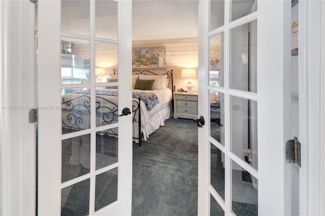 bedroom with wood walls, french doors, dark carpet, and a textured ceiling