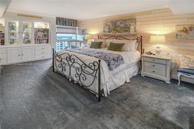 bedroom featuring dark colored carpet, wood walls, crown molding, and a textured ceiling