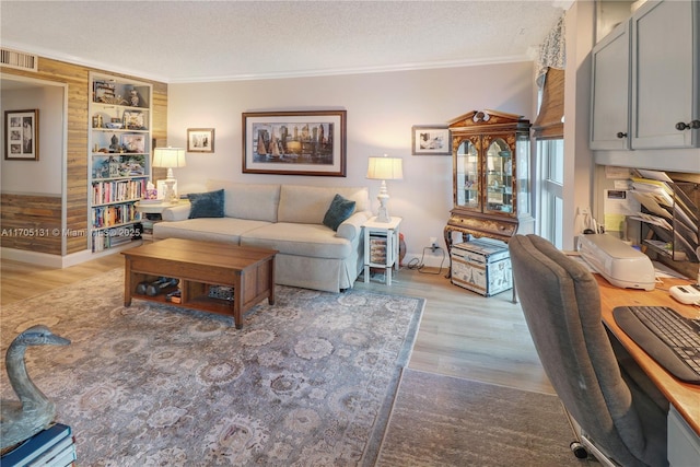 living room featuring light hardwood / wood-style floors, built in features, a textured ceiling, and ornamental molding