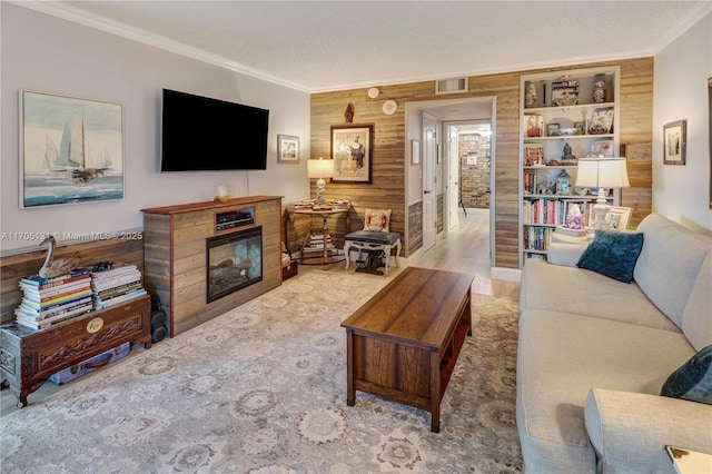 living room featuring wood walls, ornamental molding, a textured ceiling, built in features, and wood-type flooring