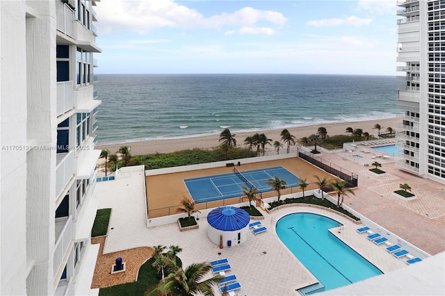 exterior space with tennis court, a water view, and a view of the beach