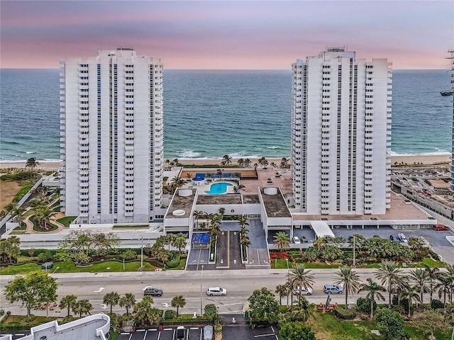 aerial view at dusk featuring a view of the beach and a water view