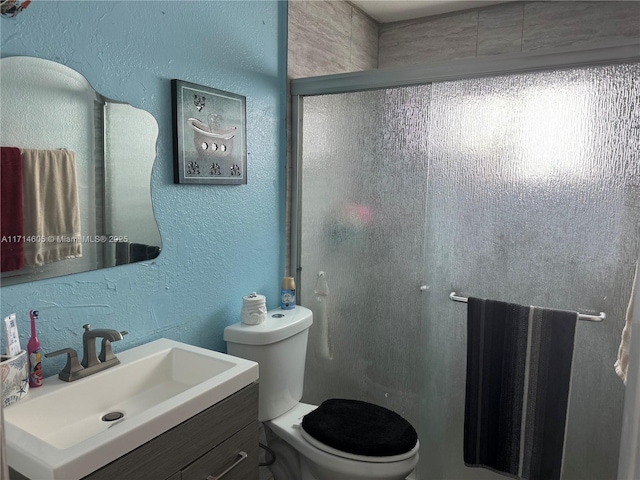 bathroom featuring a stall shower, a textured wall, vanity, and toilet