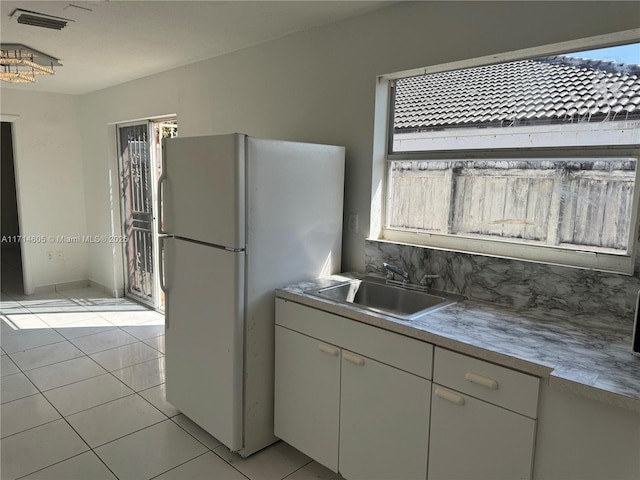 kitchen featuring light tile patterned floors, visible vents, freestanding refrigerator, a healthy amount of sunlight, and a sink