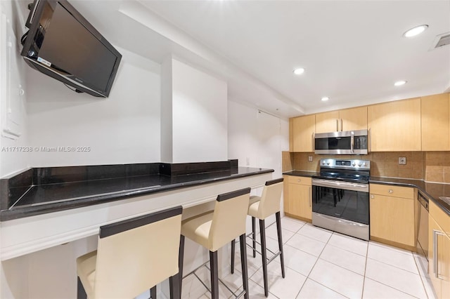 kitchen with a breakfast bar area, light brown cabinetry, and stainless steel appliances