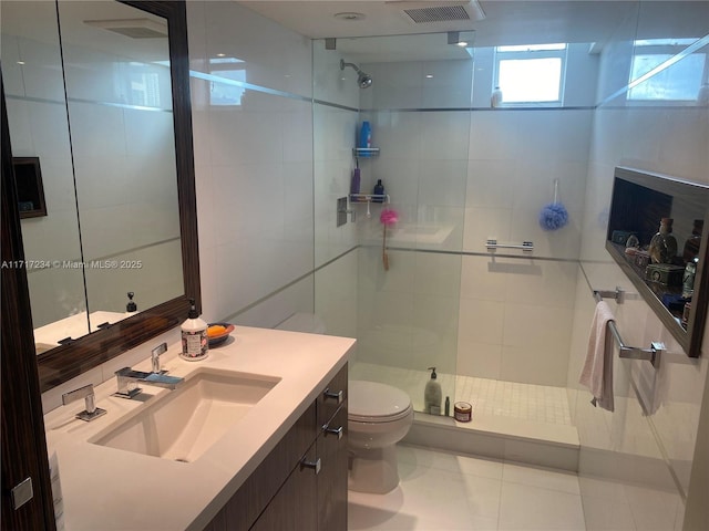 bathroom featuring tile patterned flooring, a tile shower, vanity, and toilet