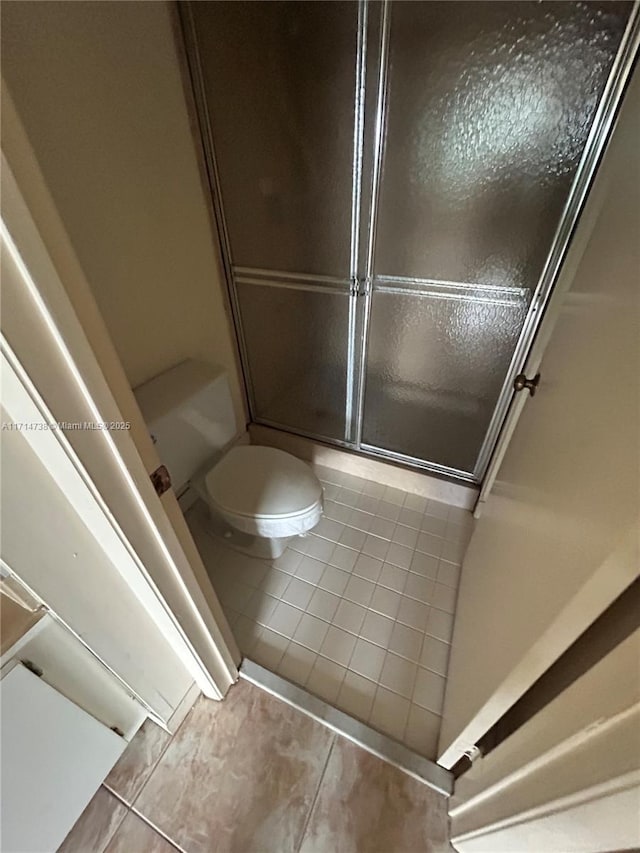 bathroom featuring tile patterned flooring, toilet, and a shower with shower door