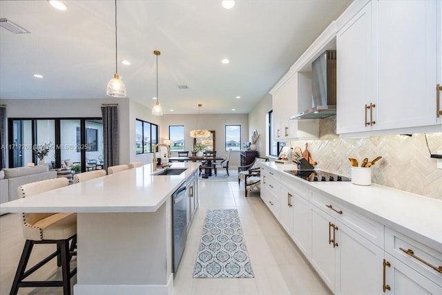 kitchen with black electric stovetop, wall chimney exhaust hood, a breakfast bar, sink, and pendant lighting