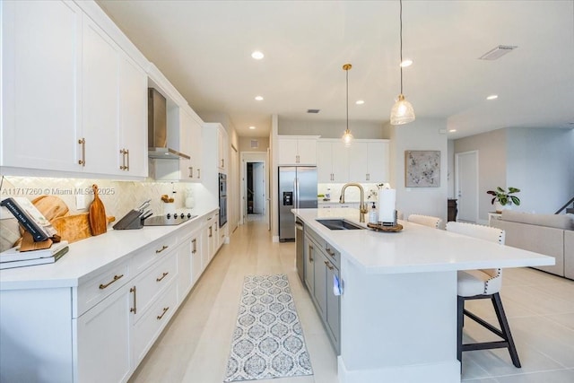 kitchen with stainless steel refrigerator with ice dispenser, tasteful backsplash, wall chimney exhaust hood, sink, and white cabinetry