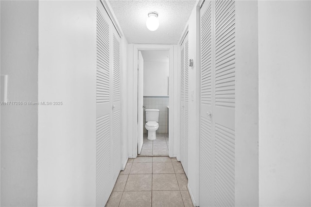 corridor featuring a textured ceiling, light tile patterned floors, and tile walls