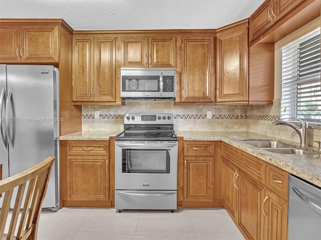 kitchen featuring sink, stainless steel appliances, tasteful backsplash, light stone counters, and light tile patterned floors