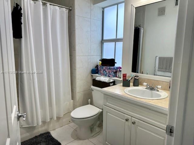 full bathroom with vanity, shower / bathtub combination with curtain, tile walls, tile patterned flooring, and toilet