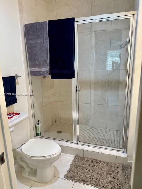 bathroom with tile patterned floors, toilet, and a shower with shower door