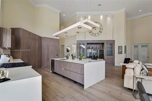 kitchen with light hardwood / wood-style floors, ornamental molding, a kitchen island with sink, and a high ceiling