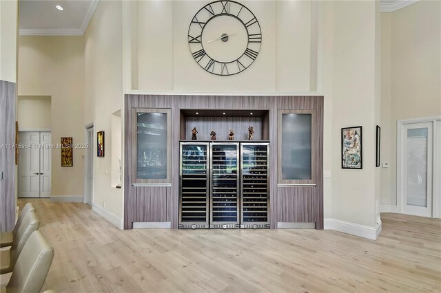 bar with light hardwood / wood-style floors, a high ceiling, and ornamental molding