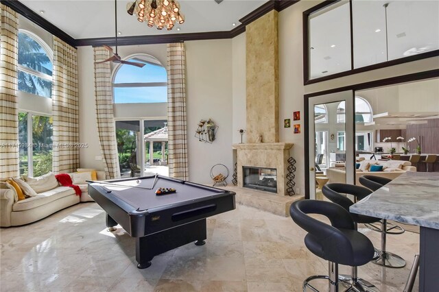 rec room featuring billiards, crown molding, a notable chandelier, a premium fireplace, and a high ceiling