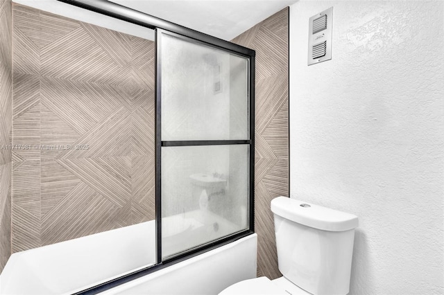 bathroom featuring toilet and bath / shower combo with glass door