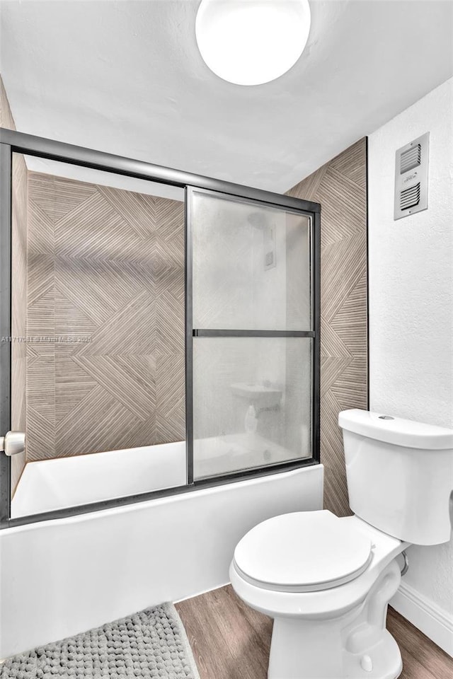 bathroom featuring combined bath / shower with glass door, wood-type flooring, and toilet