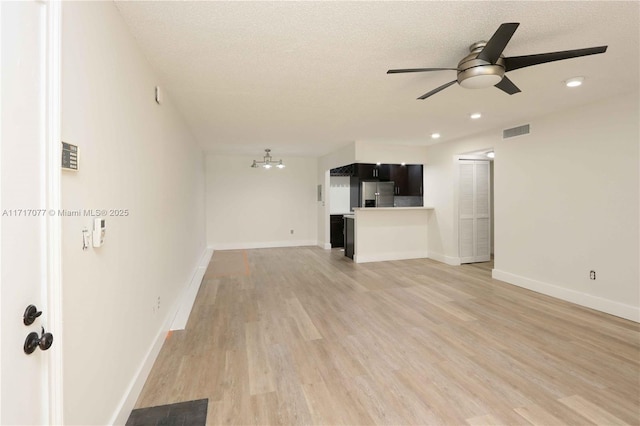 unfurnished living room with ceiling fan with notable chandelier, a textured ceiling, and light wood-type flooring