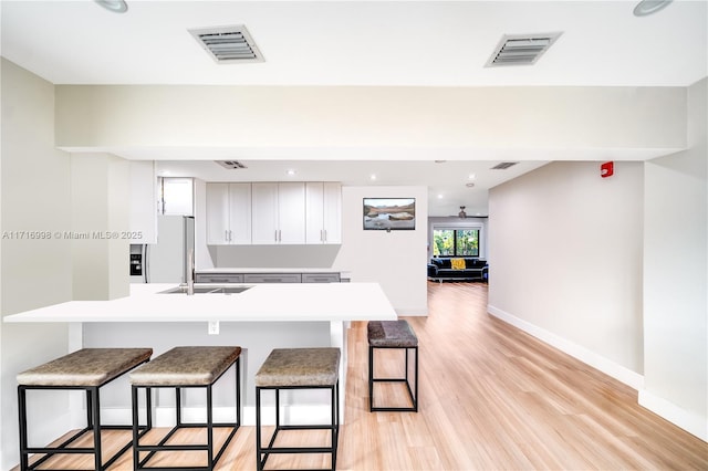 kitchen with sink, white fridge with ice dispenser, light hardwood / wood-style floors, a kitchen bar, and white cabinetry