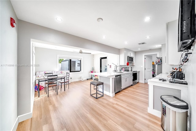 kitchen featuring ceiling fan, stainless steel appliances, a kitchen breakfast bar, white cabinets, and light wood-type flooring