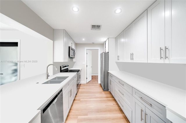 kitchen with white cabinets, appliances with stainless steel finishes, light wood-type flooring, and sink